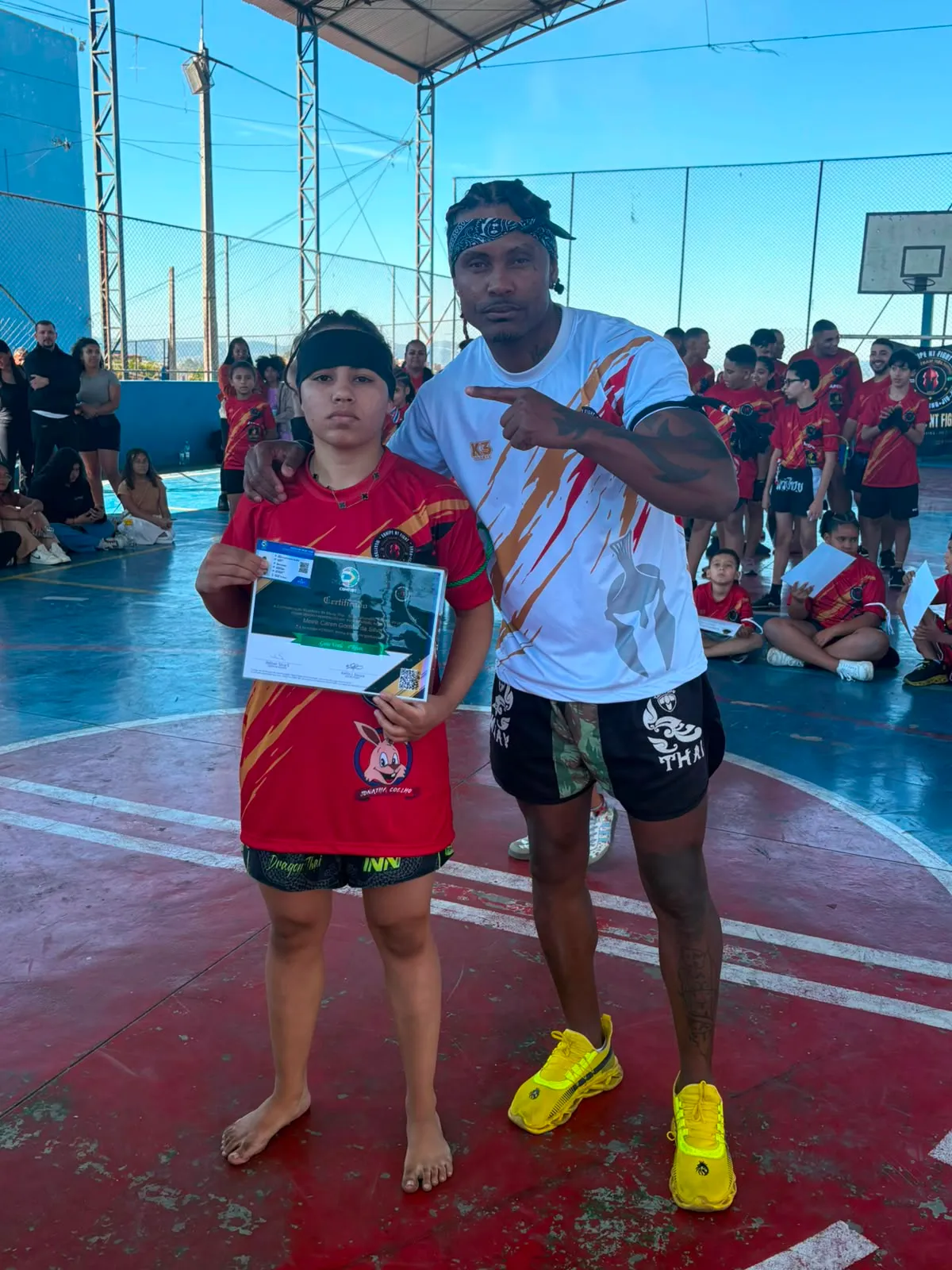 Aluno da turma kids exibindo o certificado de graduação ao lado do Prof. Nélsinho