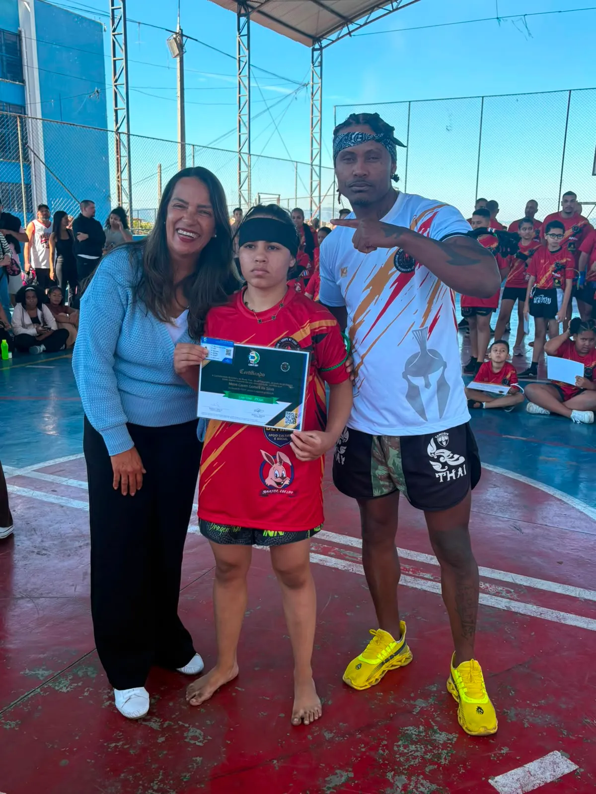 Aluno da turma kids entre a mãe e o Prof. Nélsinho, com o certificado nas mãos