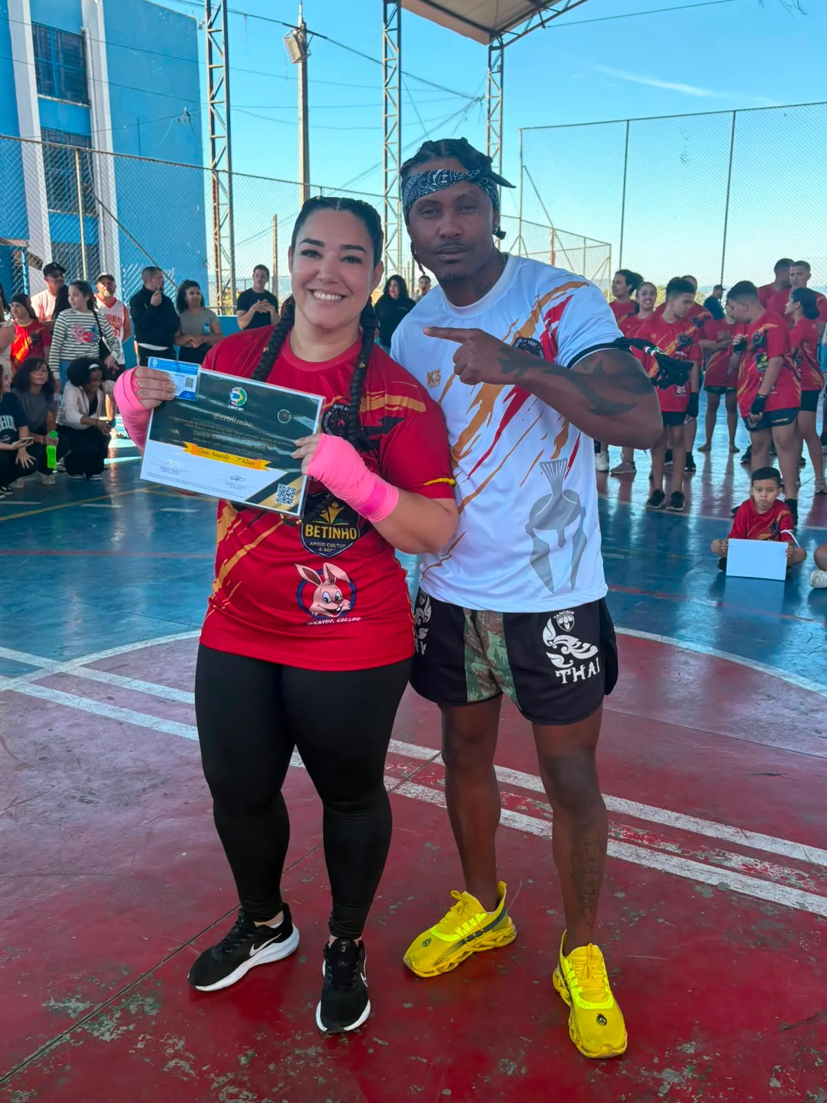 Aluno da Equipe NT Fight com o certificado de graduação ao lado do Prof. Nélsinho, na cerimônia de julho de 2026