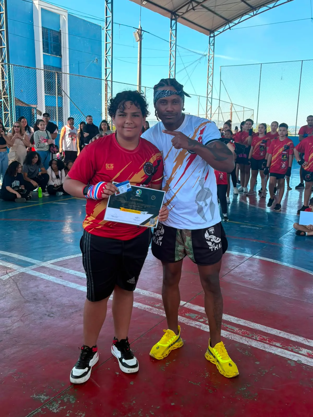 Aluno da Equipe NT Fight com o certificado de graduação ao lado do Prof. Nélsinho, na cerimônia de julho de 2026