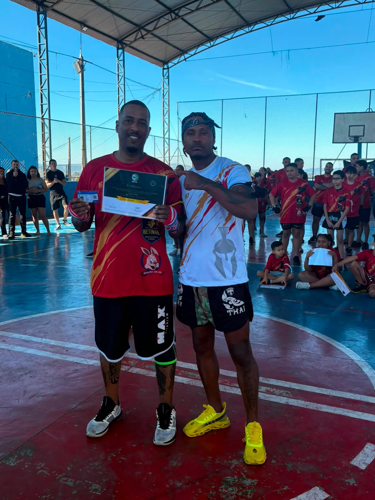 Aluno da Equipe NT Fight com o certificado de graduação ao lado do Prof. Nélsinho, na cerimônia de julho de 2026