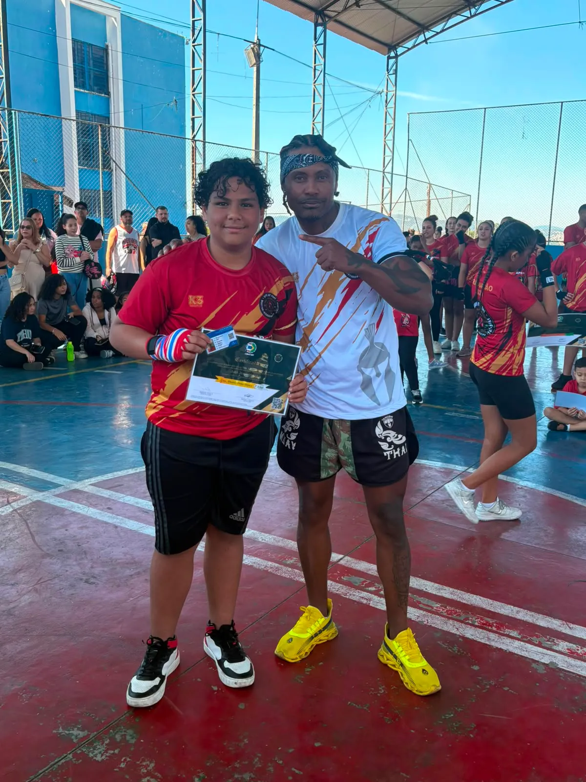 Aluno da Equipe NT Fight com o certificado de graduação ao lado do Prof. Nélsinho, na cerimônia de julho de 2026
