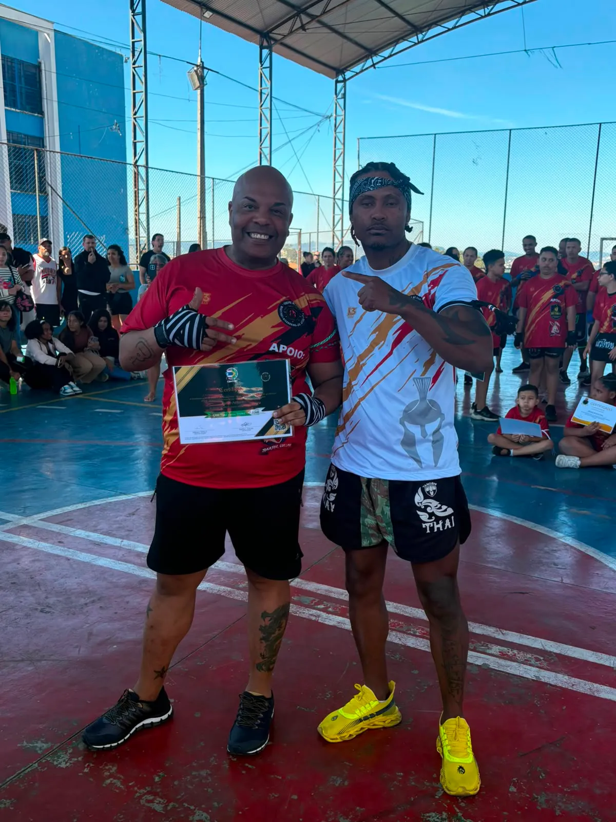 Aluno da Equipe NT Fight com o certificado de graduação ao lado do Prof. Nélsinho, na cerimônia de julho de 2026