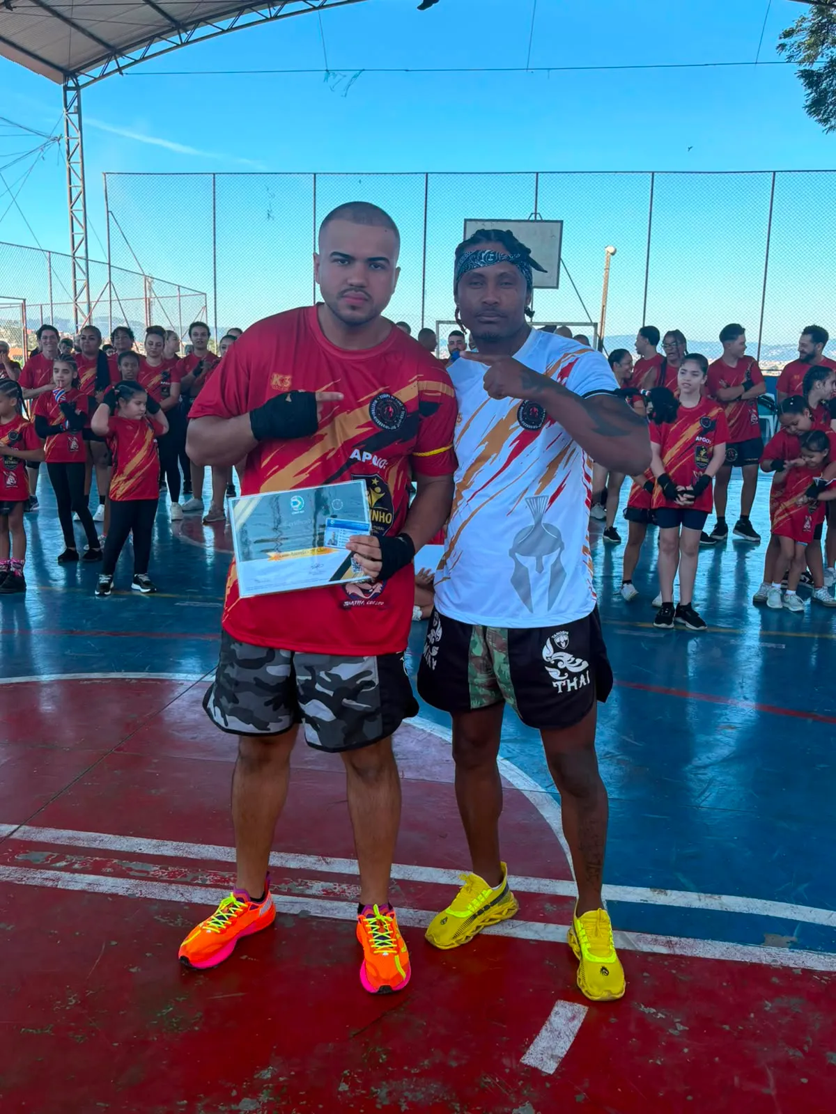Aluno da Equipe NT Fight com o certificado de graduação ao lado do Prof. Nélsinho, na cerimônia de julho de 2026