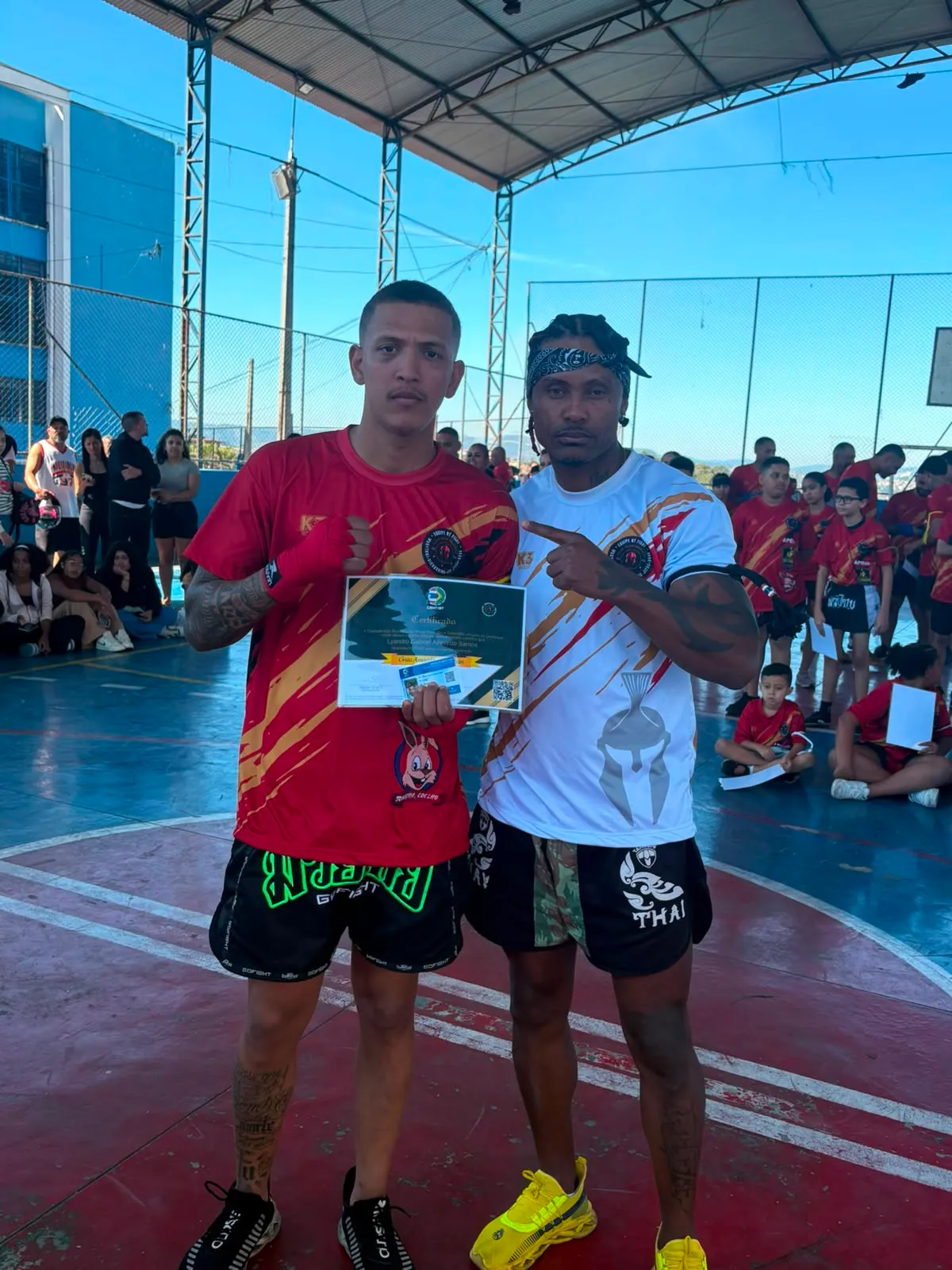 Aluno da Equipe NT Fight com o certificado de graduação ao lado do Prof. Nélsinho, na cerimônia de julho de 2026