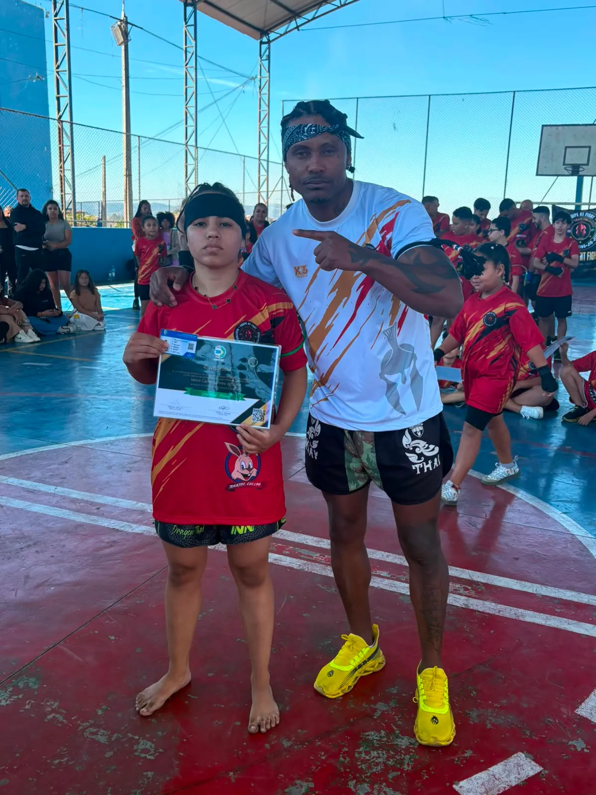 Aluno da Equipe NT Fight com o certificado de graduação ao lado do Prof. Nélsinho, na cerimônia de julho de 2026