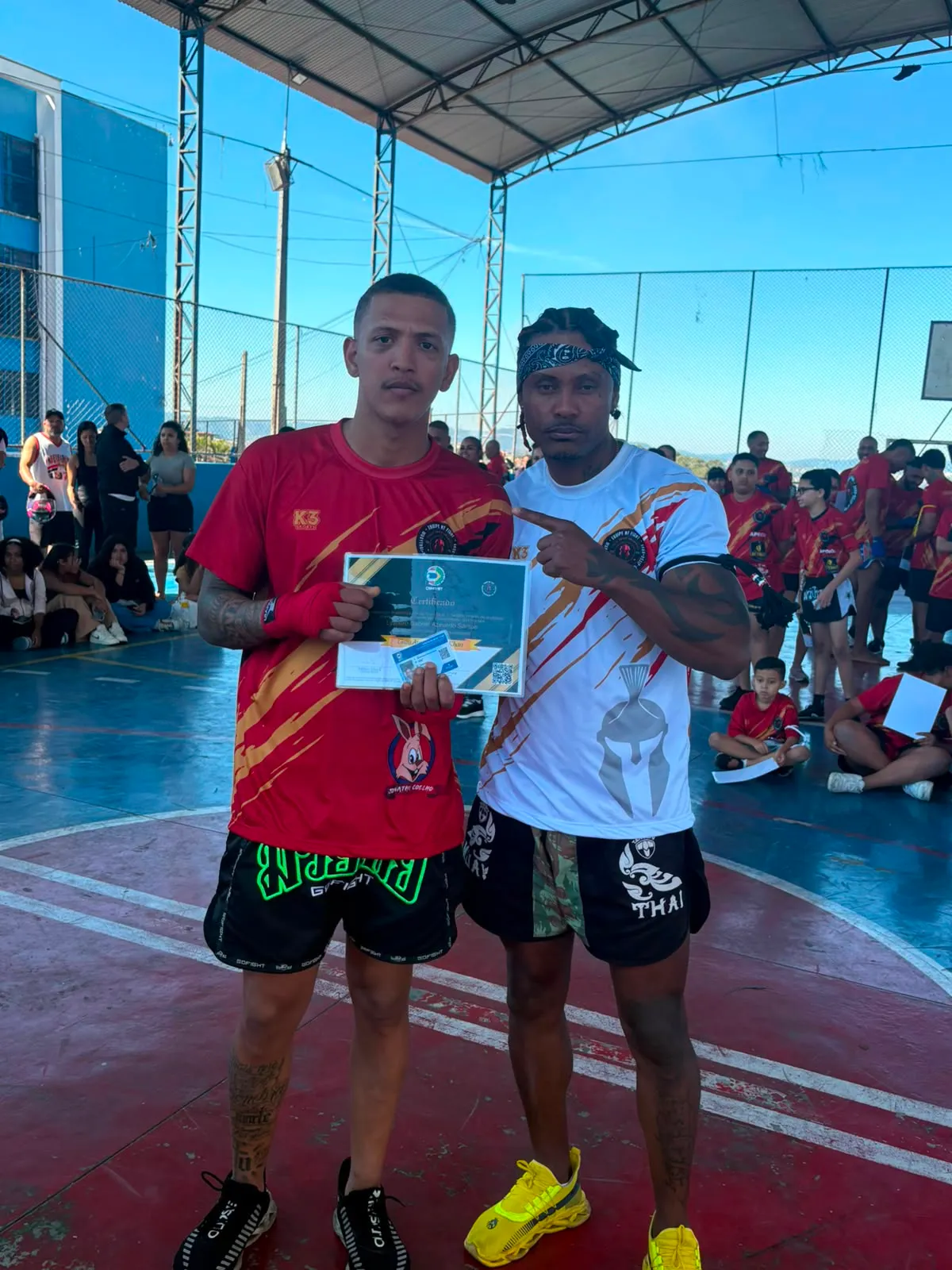 Aluno da Equipe NT Fight com o certificado de graduação ao lado do Prof. Nélsinho, na cerimônia de julho de 2026