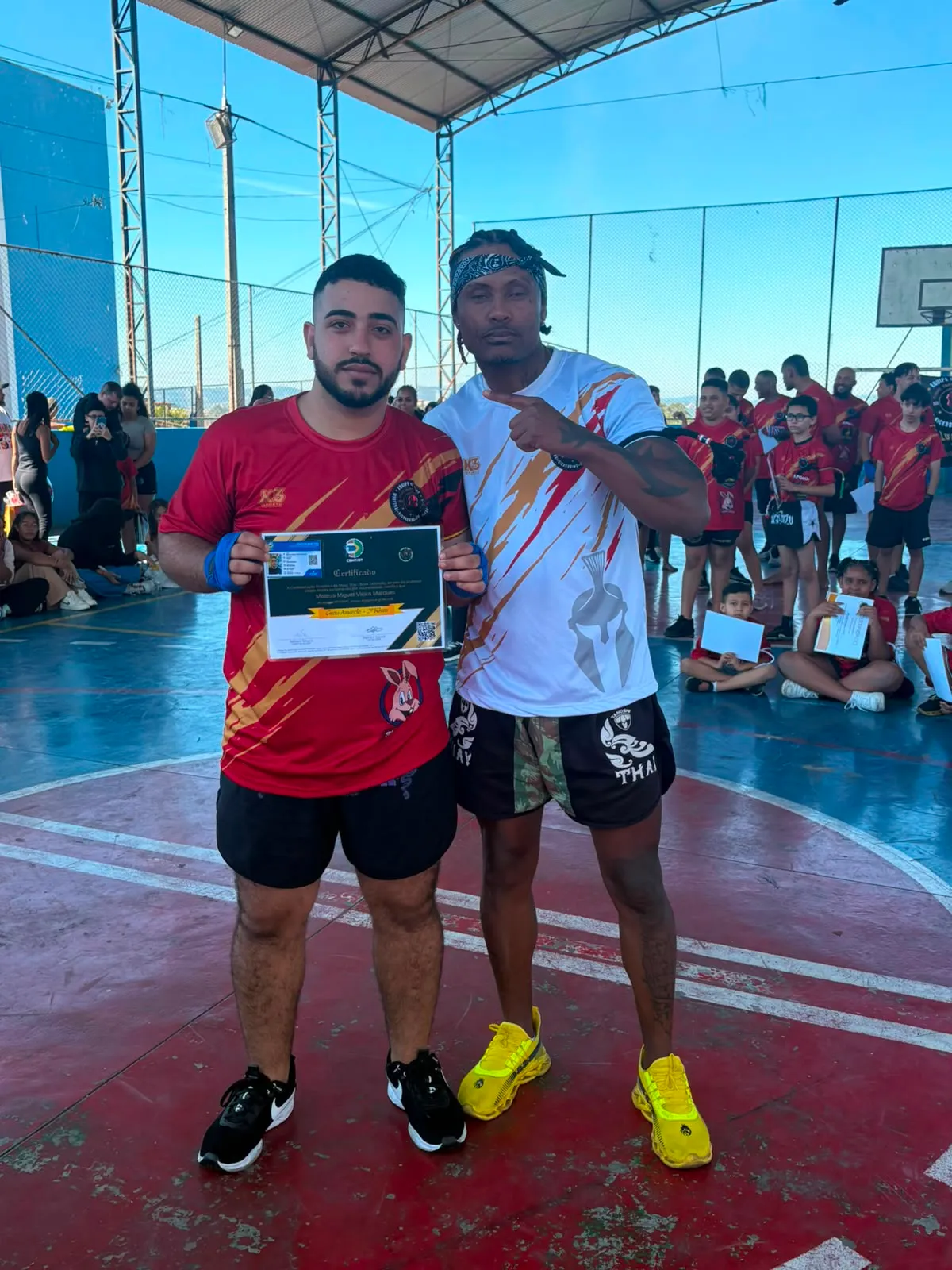 Aluno da Equipe NT Fight com o certificado de graduação ao lado do Prof. Nélsinho, na cerimônia de julho de 2026