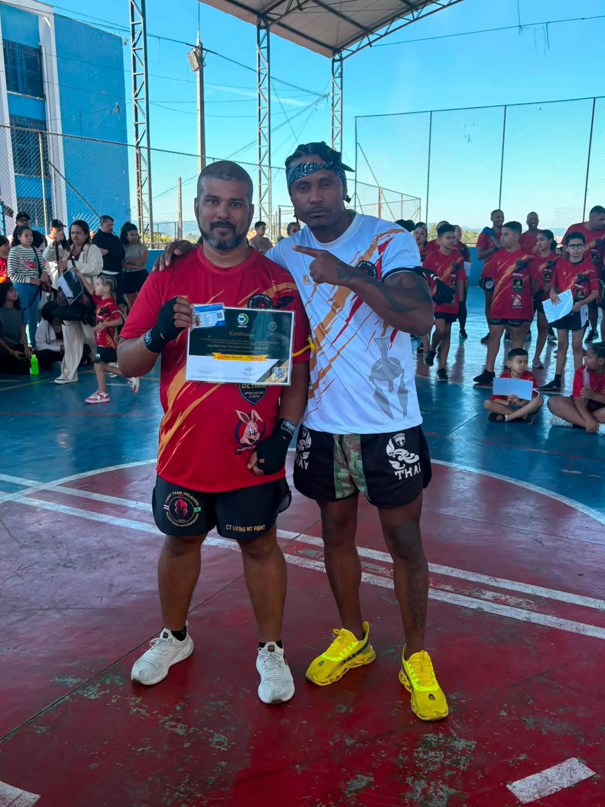 Aluno da Equipe NT Fight com o certificado de graduação ao lado do Prof. Nélsinho, na cerimônia de julho de 2026