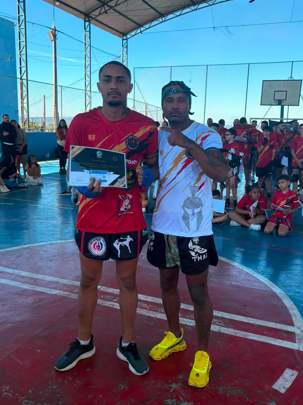 Aluno da Equipe NT Fight com o certificado de graduação ao lado do Prof. Nélsinho, na cerimônia de julho de 2026