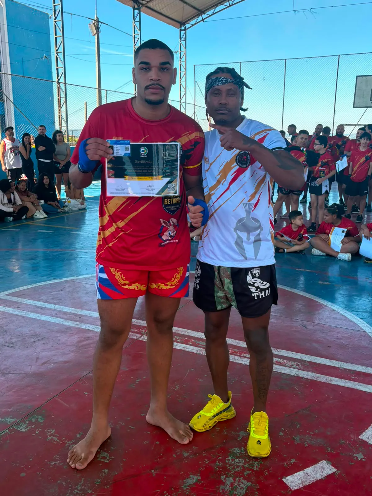 Aluno da Equipe NT Fight com o certificado de graduação ao lado do Prof. Nélsinho, na cerimônia de julho de 2026
