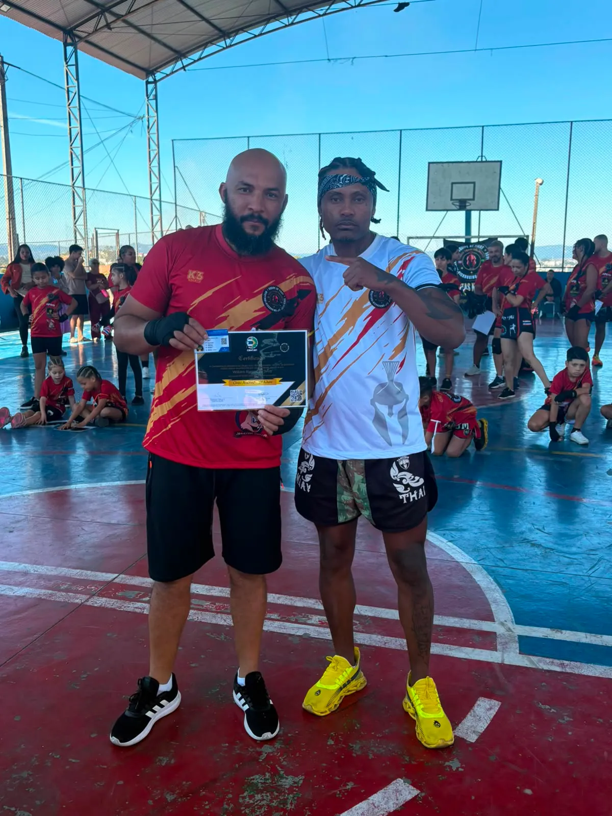 Aluno da Equipe NT Fight com o certificado de graduação ao lado do Prof. Nélsinho, na cerimônia de julho de 2026