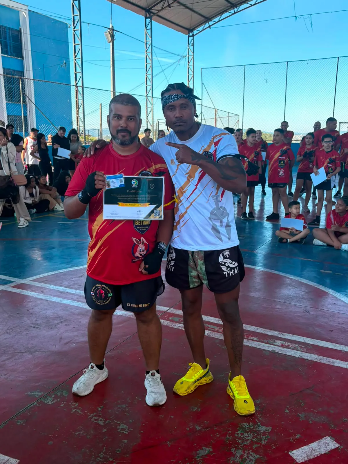 Aluno da Equipe NT Fight com o certificado de graduação ao lado do Prof. Nélsinho, na cerimônia de julho de 2026