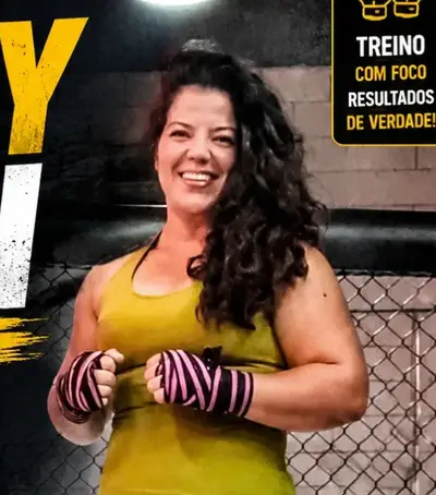 Instrutora Keilla Souza sorrindo, com bandagens rosa nas mãos, dentro do octógono