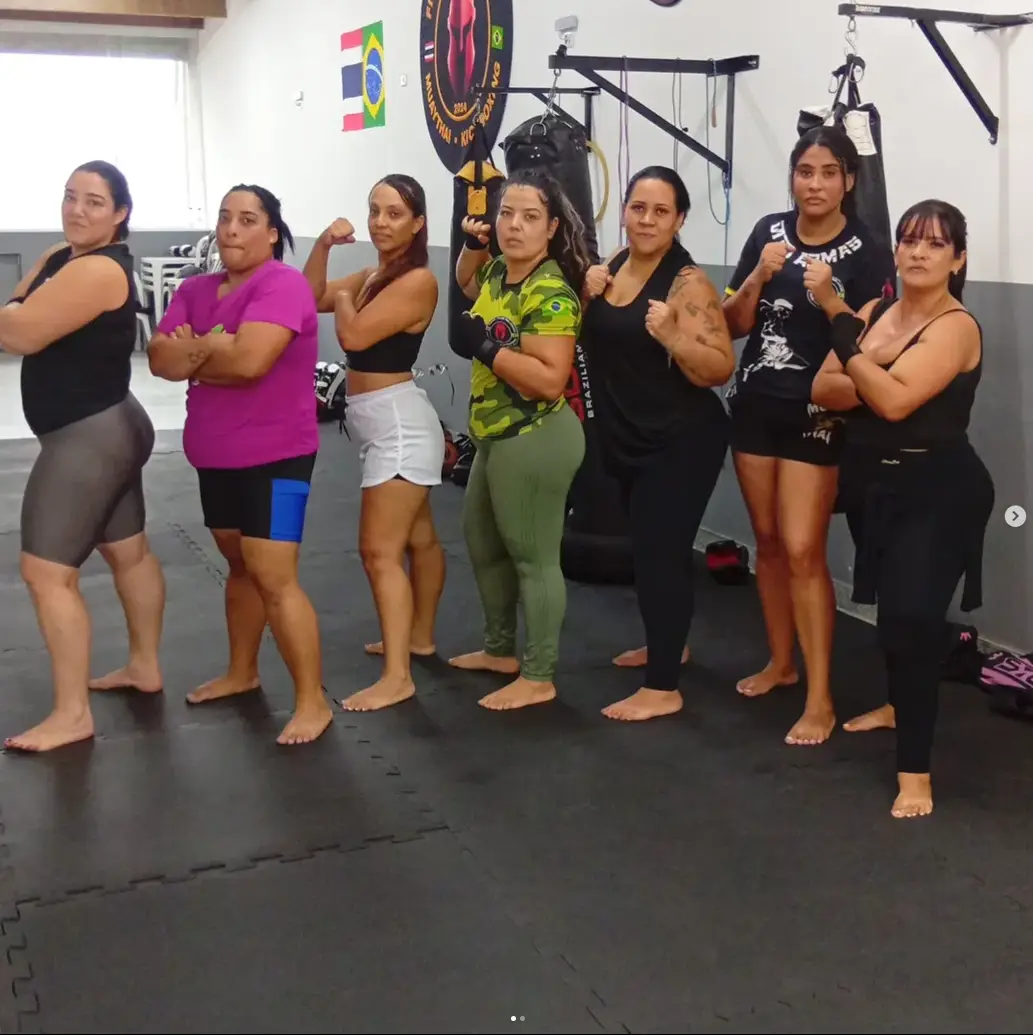 Alunas da turma feminina de Muay Thai perfiladas em guarda diante do saco de pancadas