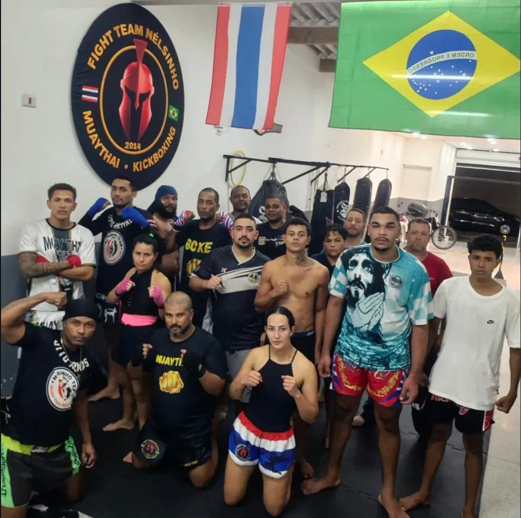 Turma da Equipe NT Fight reunida no CT, sob o brasão da equipe e as bandeiras do Brasil e da Tailândia
