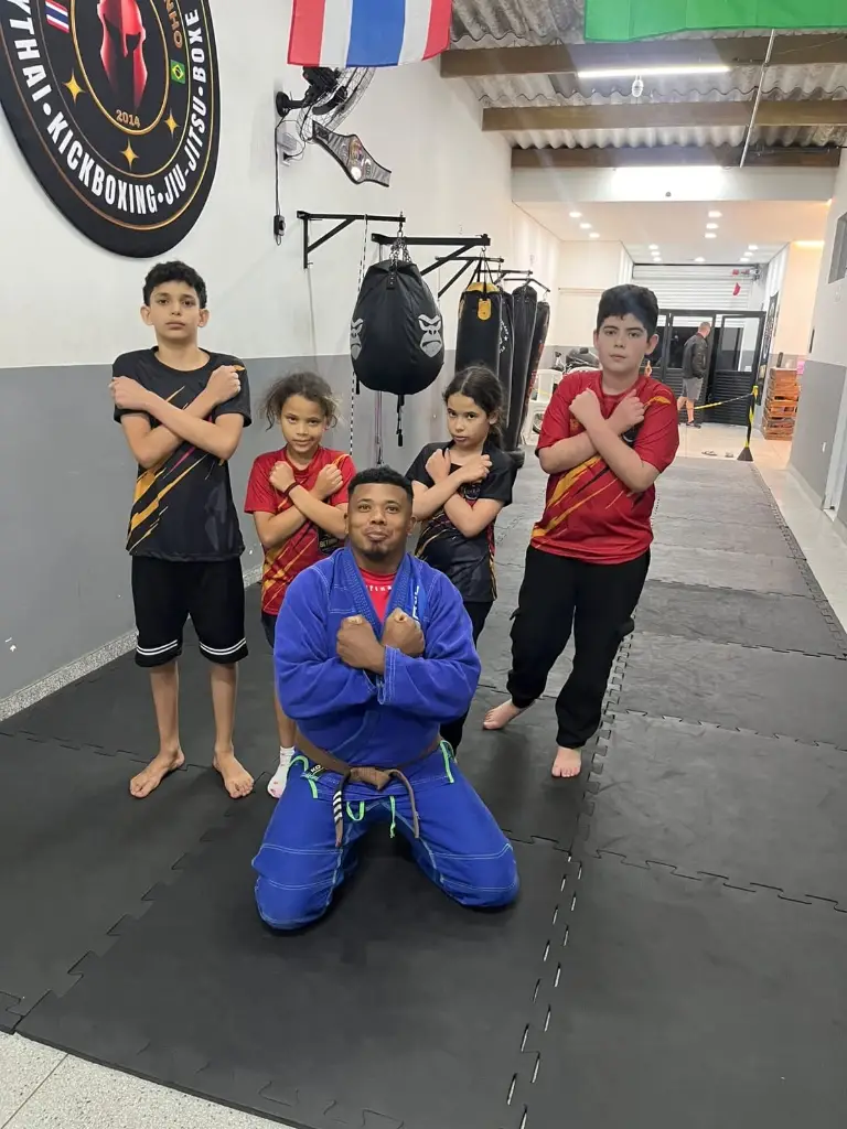 Prof. Kleiton de quimono azul e alunos da turma de Jiu-Jitsu perfilados no tatame da Equipe NT Fight