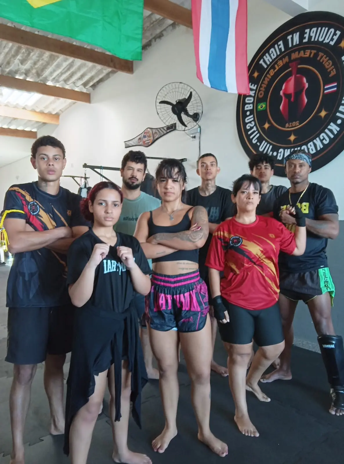 Alunos e alunas em guarda diante do brasão da Equipe NT Fight na parede