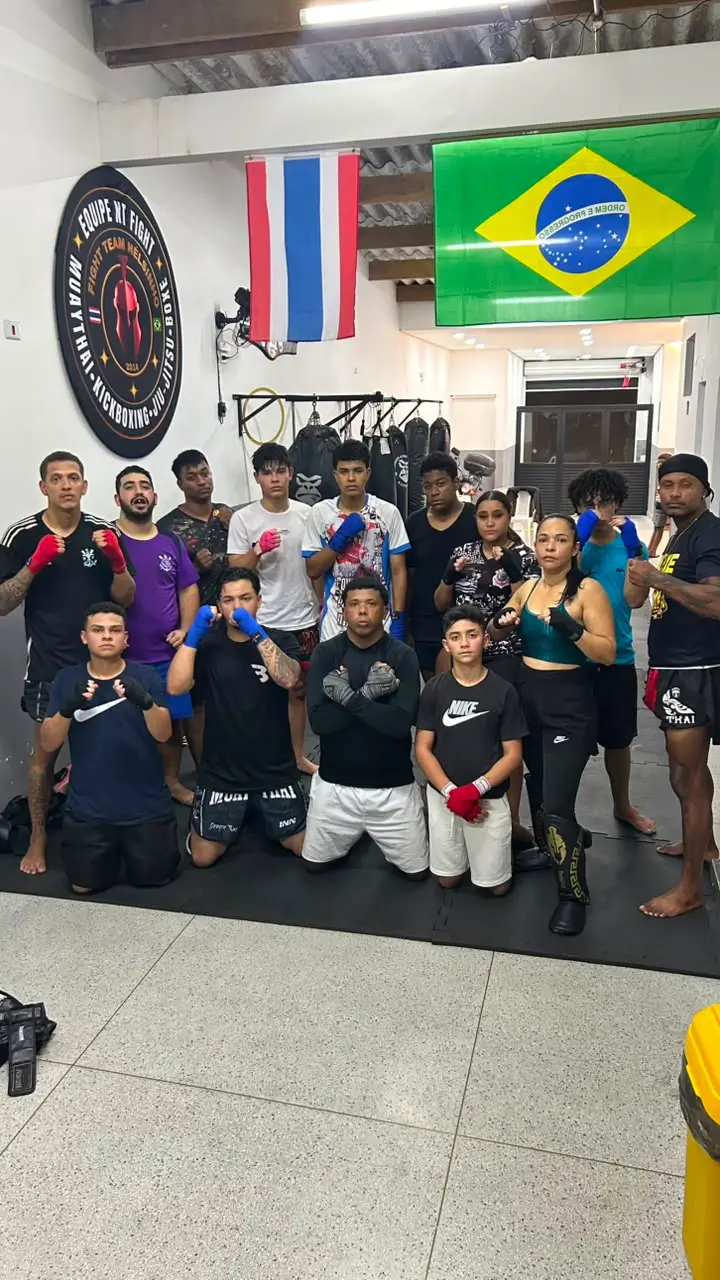 Turma de adultos e adolescentes com bandagens nas mãos, perfilada no tatame