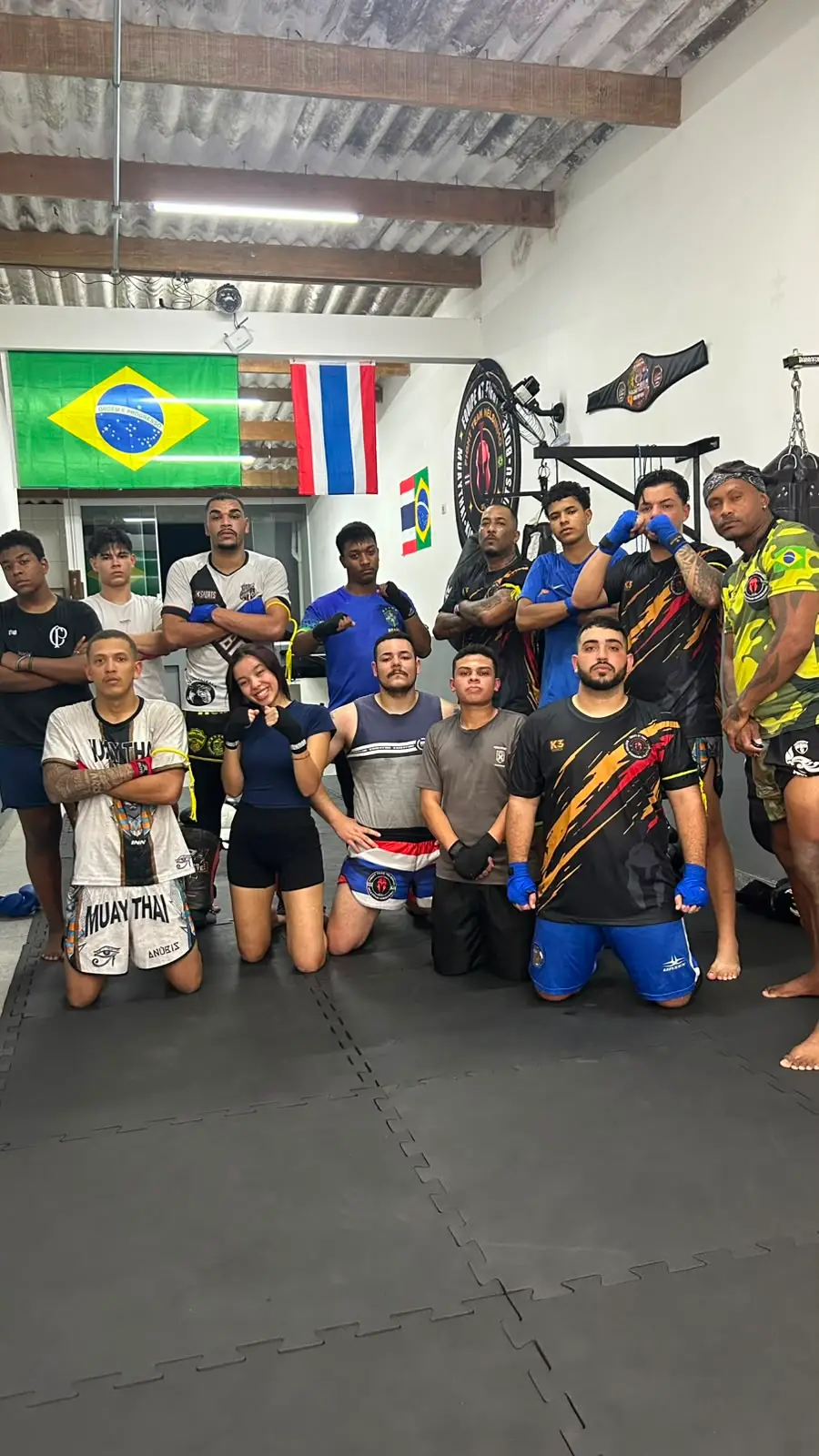 Turma cheia reunida no tatame do CT sob as bandeiras do Brasil e da Tailândia